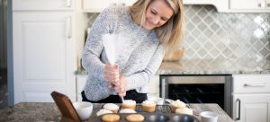 image of woman piping frosting onto cupcakes in a grey and white kitchen