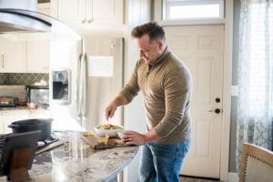 image of man drizzling dressing on a salad in a sunny kitchen