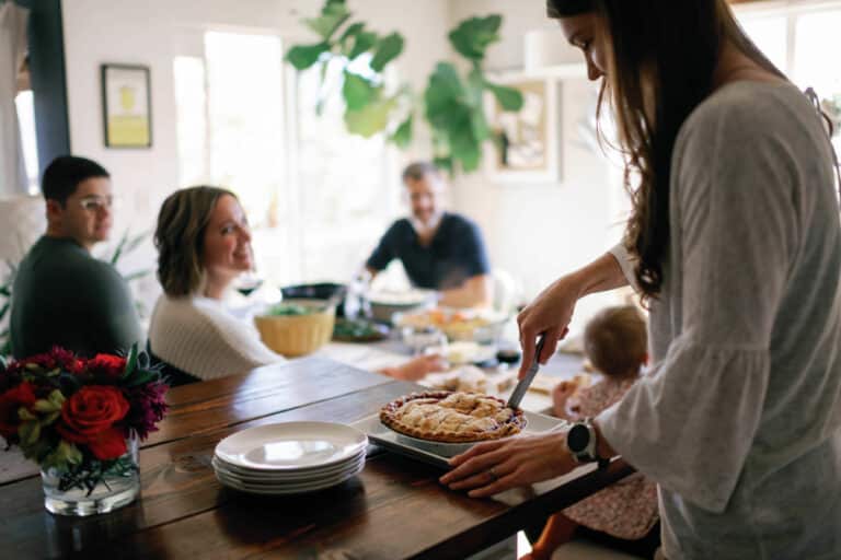 woman cutting pie with table full of people in the background