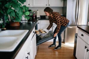 side view of woman taking a tray of baked goods out of the oven