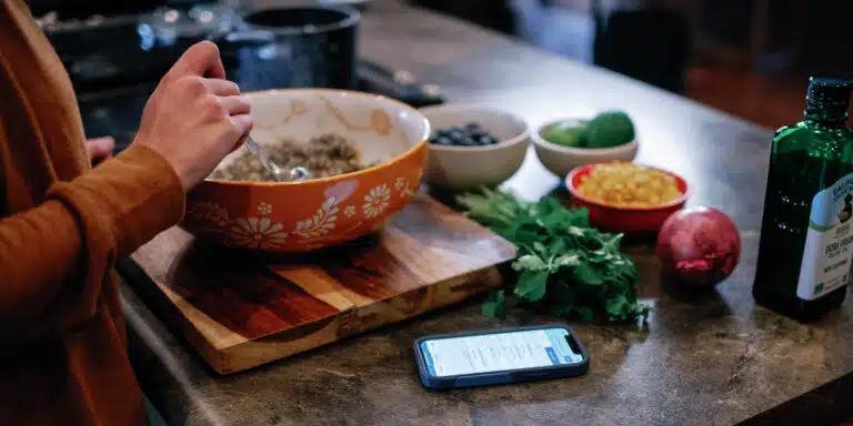 cropped image of a woman making salad with ingredients on the counter and phone