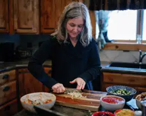 middle-aged woman chopping vegetables in a black sweater