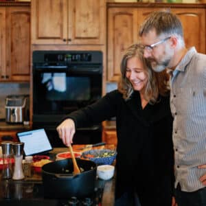 Clint and Lisa cooking together in a kitchen with wood cabinets
