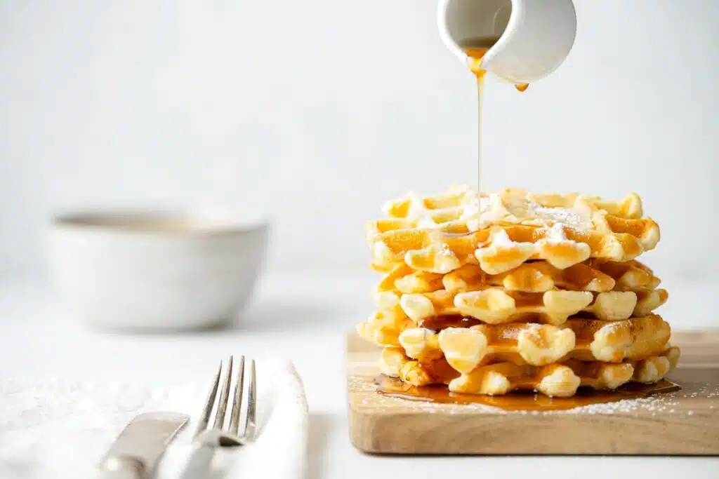 side view of a stack of waffles with syrup being poured over the top