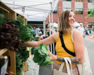 image of woman in yellow shirt grabbing lettuce from a stall at the farmer's market