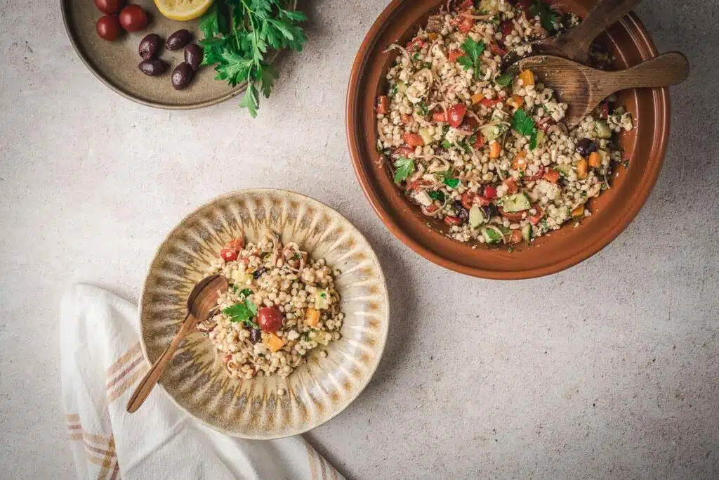 overhead shot of couscous in a brown bowl with a separate portion in a smaller bowl with a wooden spoon