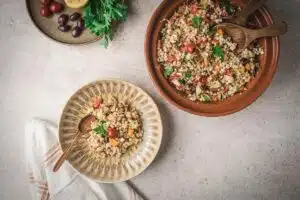 overhead shot of couscous in a brown bowl with a separate portion in a smaller bowl with a wooden spoon