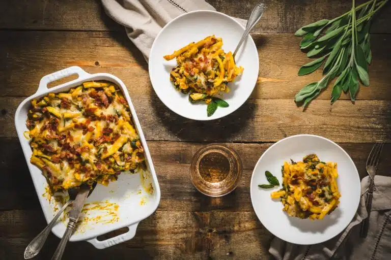 overhead view of pumpkin pasta in casserole dish with two plates of pasta servings