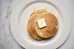 overhead shot of sourdough pancakes on a white plate, drizzled with honey and a pad of butter on top