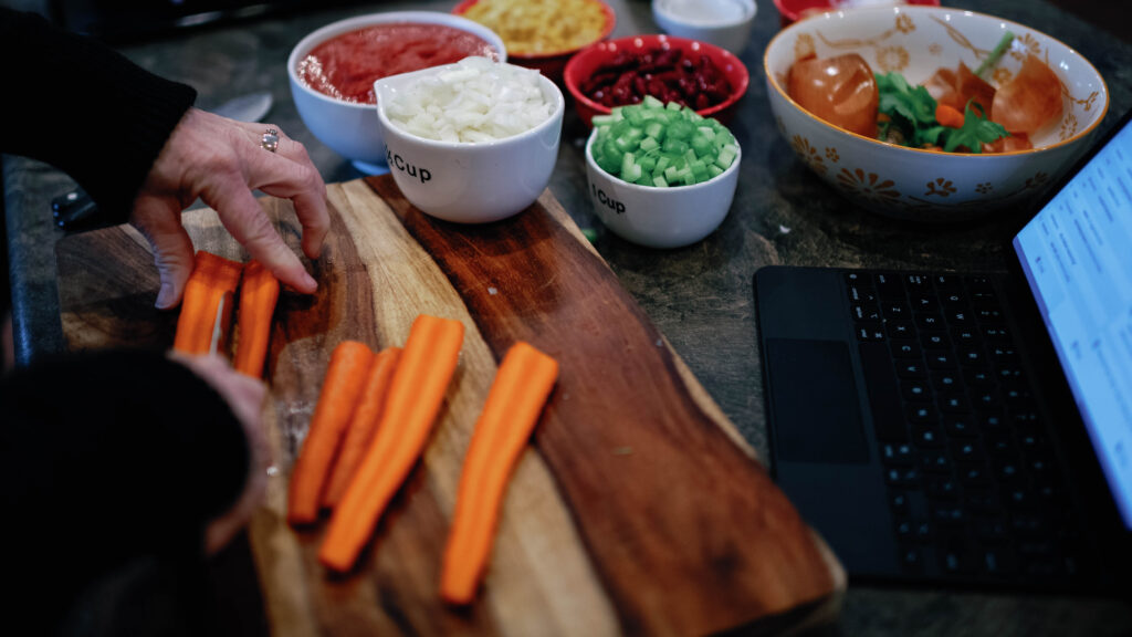 side view of woman chopping carrots on a cutting board with other cut vegetables in bowls